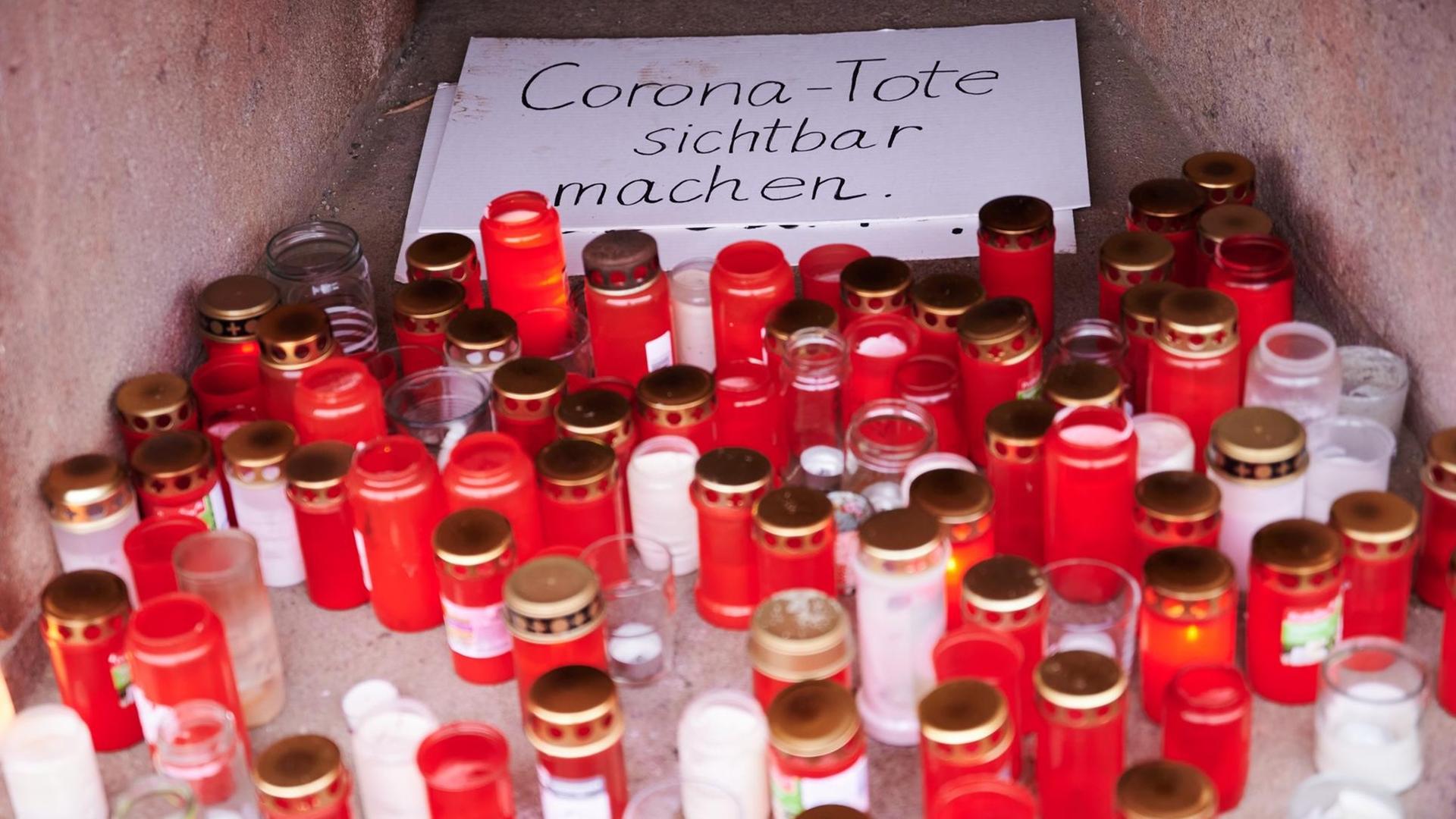 "Corona-Tote sichtbar machen" steht auf einem Karton, der von Totenlämpchen umringt ist. Eine private Initiative erinnert so an die aktuelle Zahl der Corona-Toten.