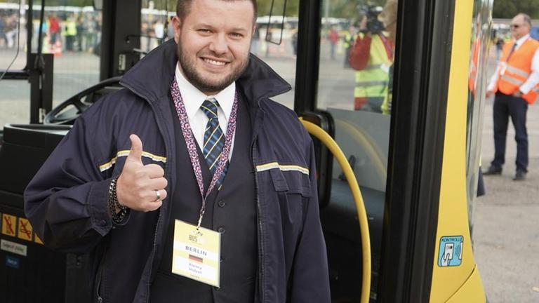 Ronny Hölzel steht vor dem Eingang seines Busses, lächelt in die Kamera und hält den Daumen hoch.