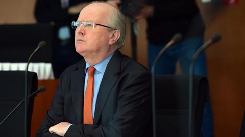 Fritsche sitzt mit verschränkten Armen und ernstem Blick an einem Tisch vor einem Mikrofon.