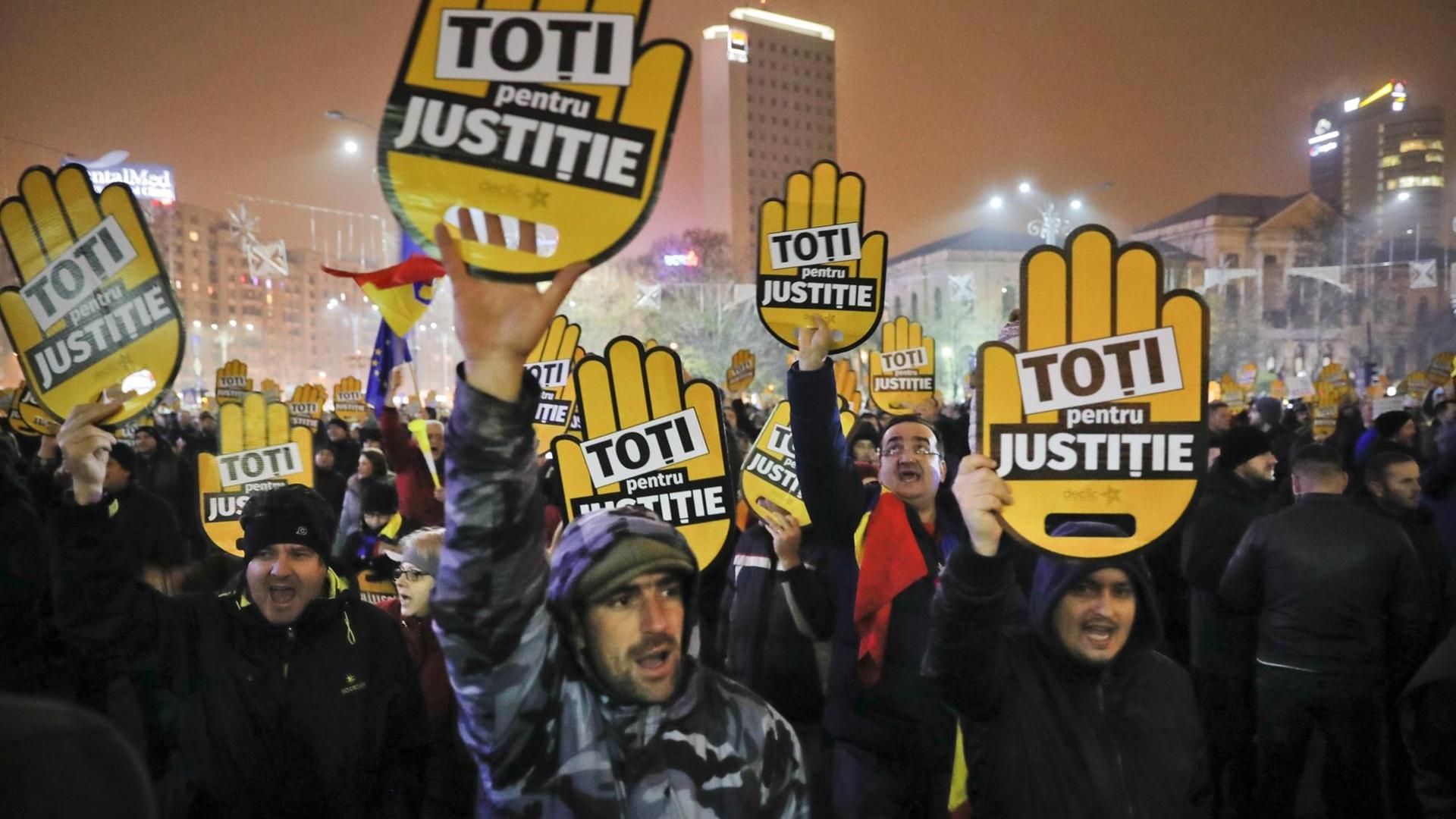 Demonstranten halten Plakate mit der Aufschrift "Alle für Gerechtigkeit" bei Straßenprotesten in Rumänien in die Höhe.