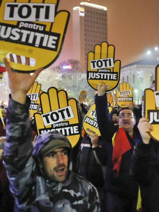 Demonstranten halten Plakate mit der Aufschrift "Alle für Gerechtigkeit" bei Straßenprotesten in Rumänien in die Höhe.