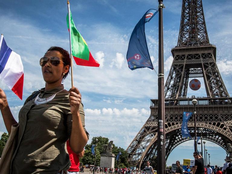 Eine Frau mit einer französischen und einer portugiesischen Flagge in der Hand läuft vor dem Eiffelturm entlang.