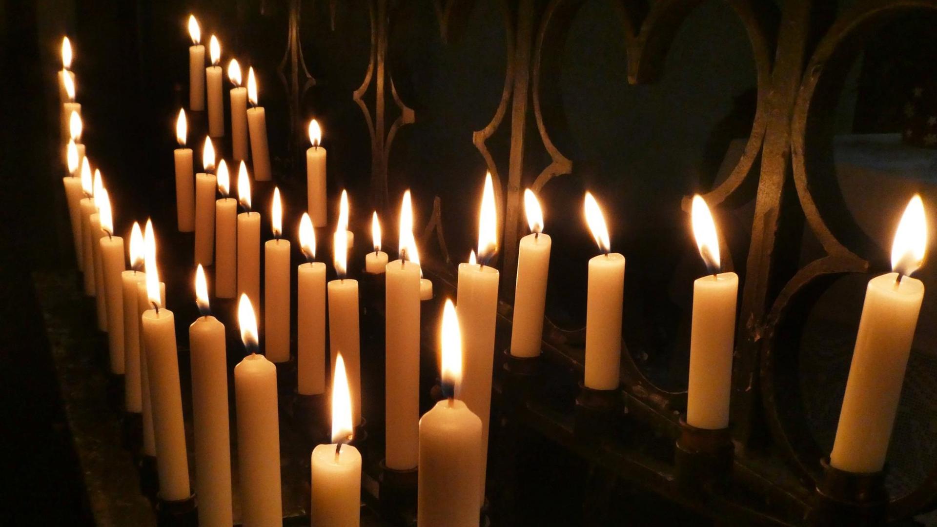 Einige Kerzen brennen in einer dunklen Ecke einer Kirche.