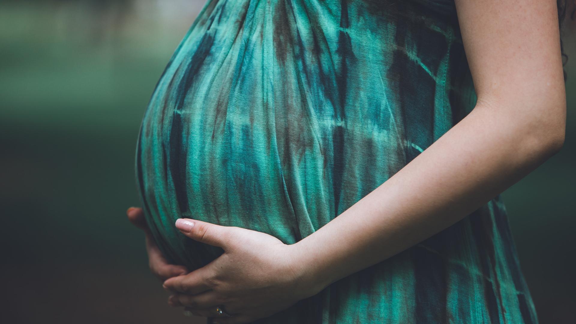 Eine schwangere Frau hält ihren Babybauch.