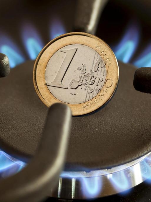 Eine Euro-Münze auf einem Gasherd mit blau leuchtender Gasflamme.