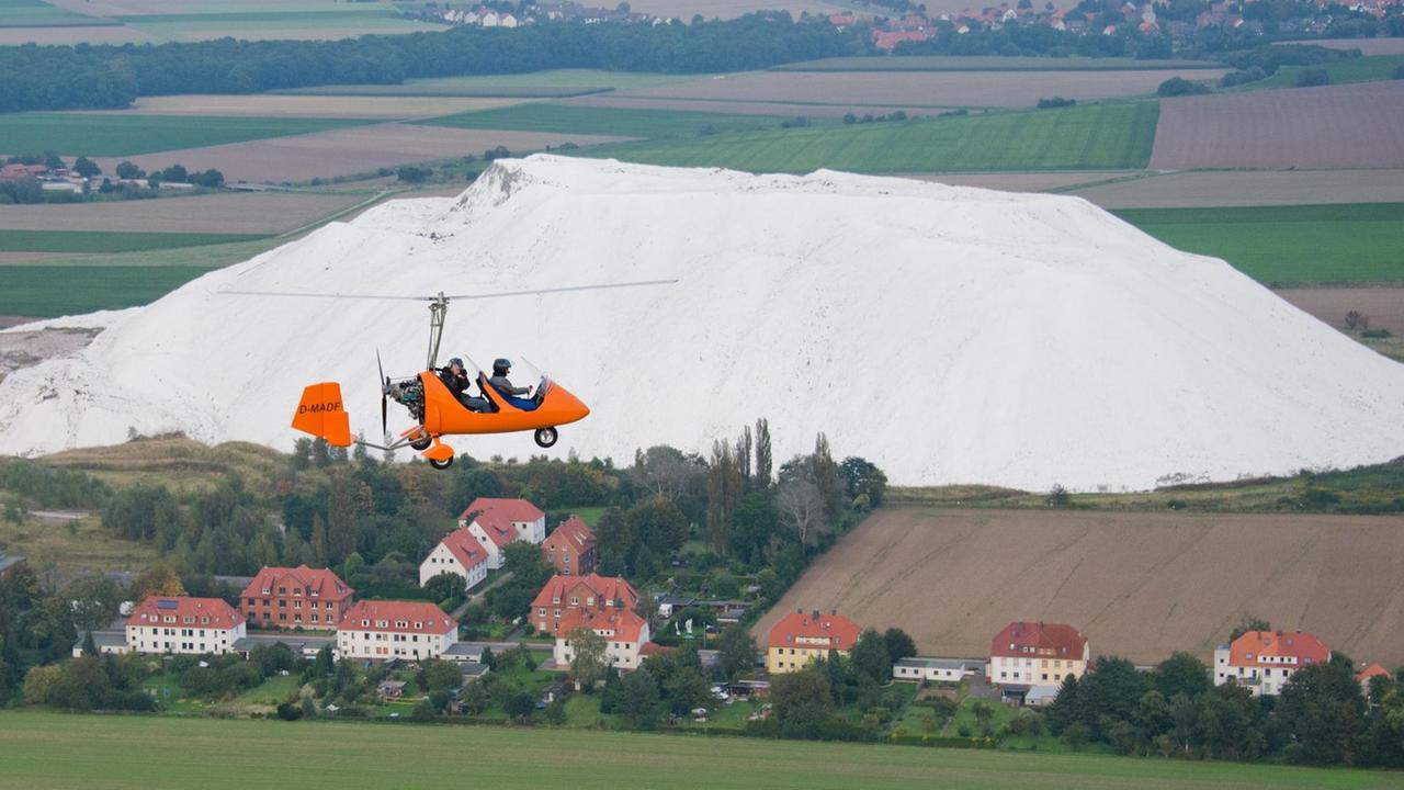 Ein Ultraleichtflugzeug Gyrocopter fliegt über einen Kaliberg in Giesen im Landkreis Hildesheim. 
