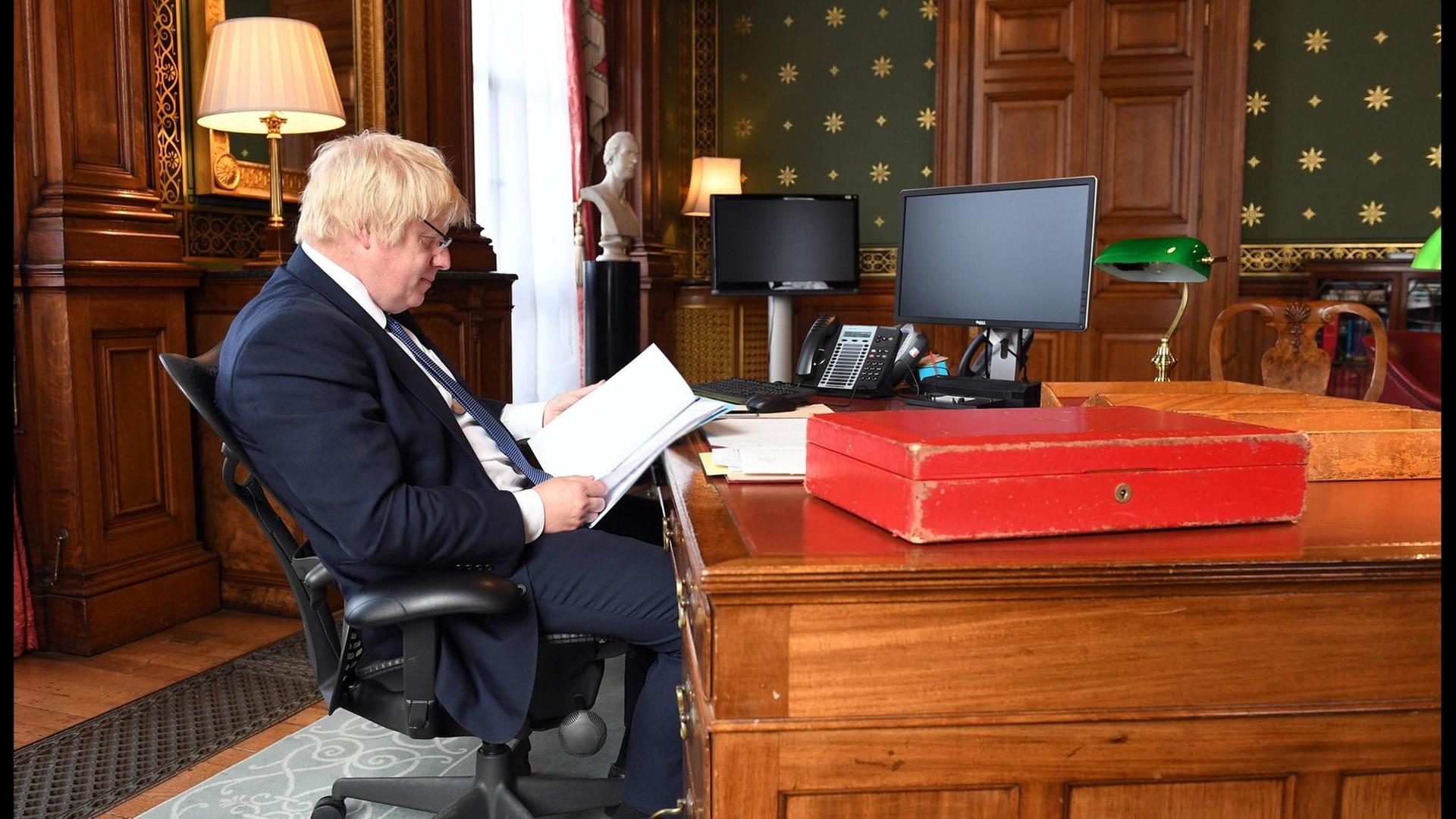 Boris Johnson sitzt an einem Schreibtisch und liest