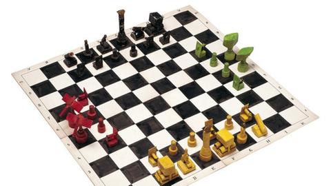 Selbst gebastelte Figuren stehen in Farbengruppen auf einem Schachbrett für ein Spiel bereit.