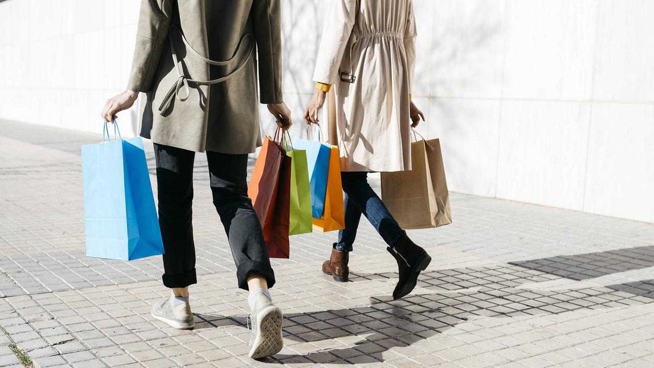 Zwei Frauen laufen mit bunten Einkaufstüten in den Händen nebeneinander.