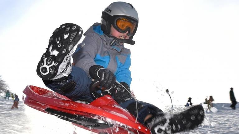 Ein Junge fährt mit einem Plastik-Bob über eine kleine Schneeschanze.