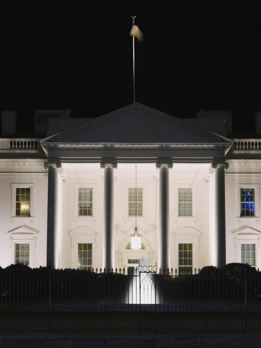 Das White House in Washington DC bei Nacht, in einem Fenster scheint Licht.