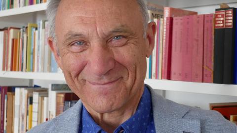 Ein Mann mit grauen Haaren blickt lächelnd in die Kamera, im Hintergrund eine Bücherwand.