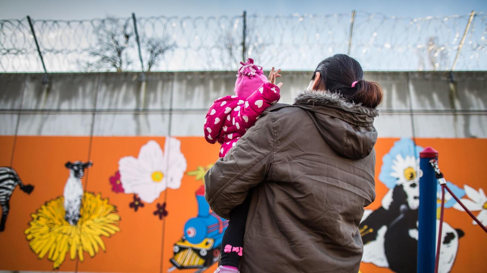 Eine Gefangene steht in Frankfurt am Main in einer Justizvollzugsanstalt mit ihrer kleinen Tochter auf dem Arm vor der bunt bemalten Gefängnismauer.