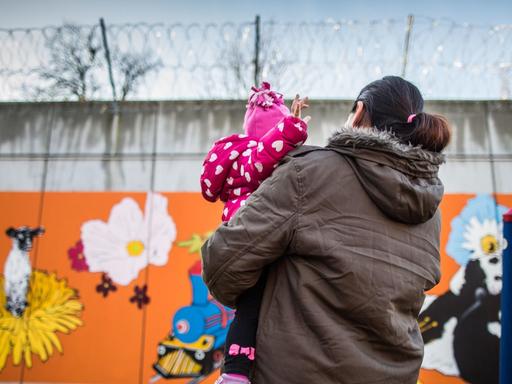 Eine Gefangene steht in Frankfurt am Main in einer Justizvollzugsanstalt mit ihrer kleinen Tochter auf dem Arm vor der bunt bemalten Gefängnismauer.