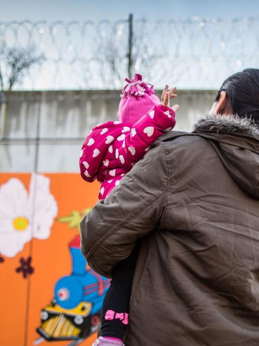 Eine Gefangene steht in Frankfurt am Main in einer Justizvollzugsanstalt mit ihrer kleinen Tochter auf dem Arm vor der bunt bemalten Gefängnismauer.