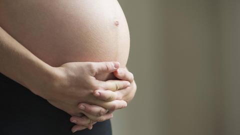 Die Hand einer schwangeren Frau auf ihrem nacktem Bauch.