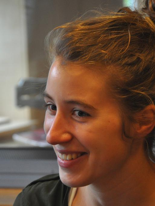 Eine junge Frau mit lockigen Haaren sitzt lächelnd in einem Tonstudio.