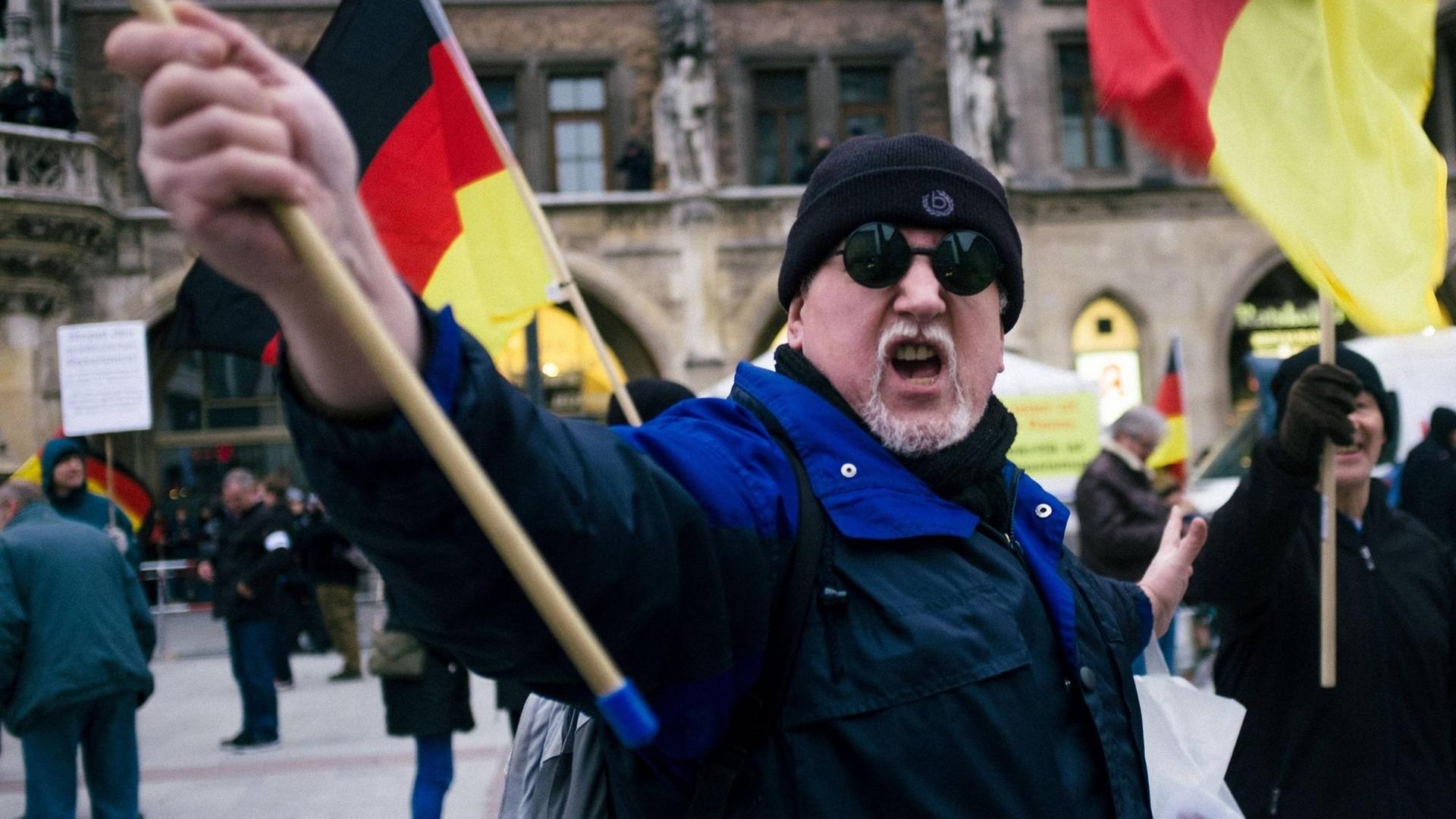 Ein vermummter Pegida-Demonstrant schwenkt eine Deutschland-Fahne.