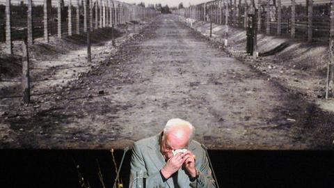 Der Auschwitz-Überlebende Kurt Julius Goldstein wischt sich auf der Gedenkveranstaltung des Internationalen Auschwitz Komitees zur Befreiung des Konzentrationslagers durch die sowjetische Armee mit einem Taschentuch Tränen aus dem Auge. Im Hintergrund ist ein großformatiges Foto des Weges zu sehen, der zu den Krematorien und Gaskammern des Vernichtungslagers führte.