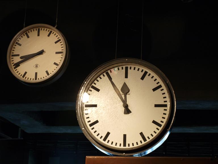 Blick auf zwei Uhren, eine zeigt fünf vor 12.