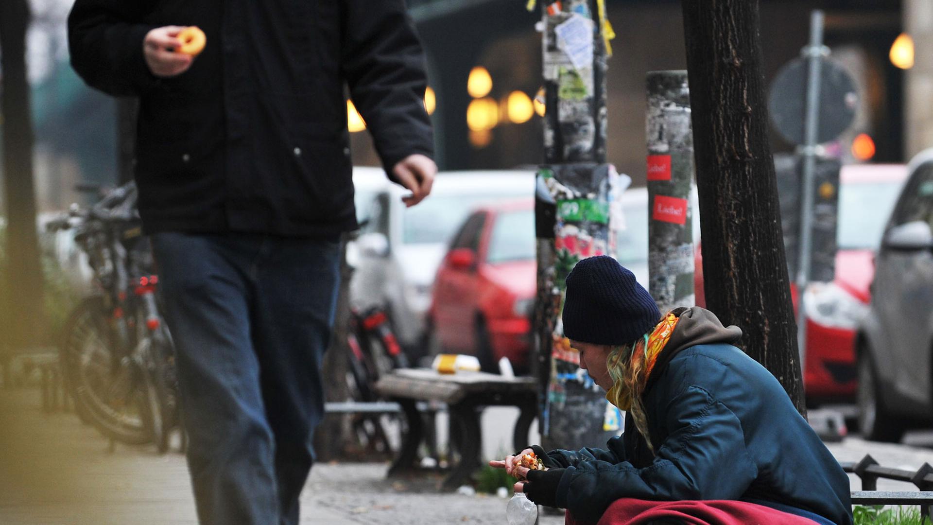 Auf einem Bürgersteig sitzt ein Obdachloser mit Hund und bettelt