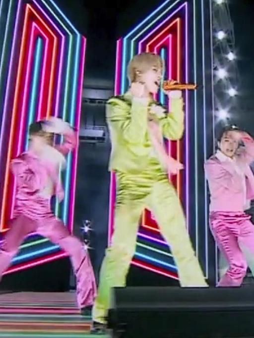 Die Mitglieder der K-Pop-Band BTS tanzen in pastellfarbenen Anzügen auf einer Bühne.