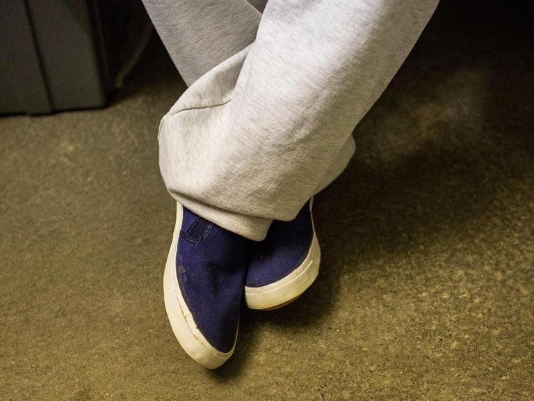 Nahaufnahme der Beine und Schuhe eines Gefangenen in seiner Zelle.