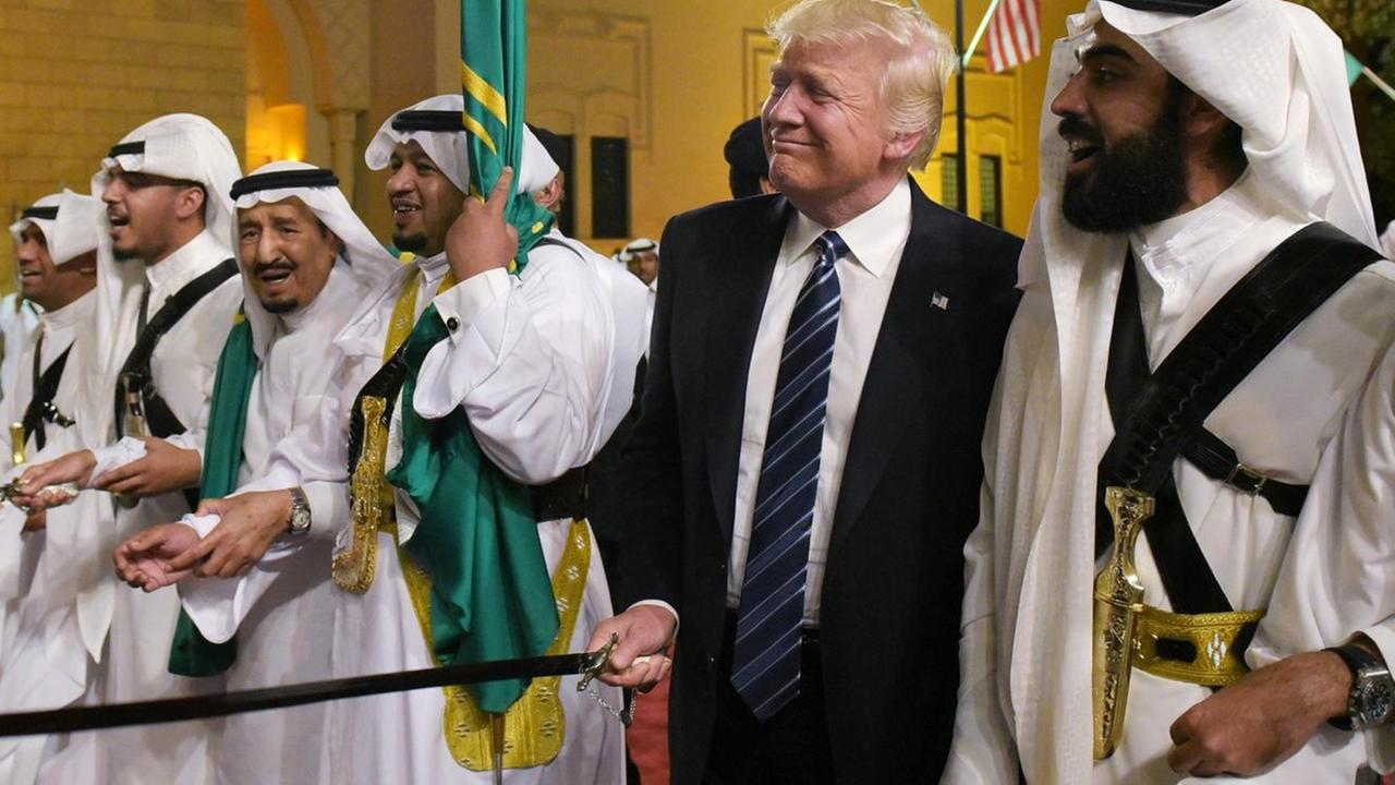 Trump steht mit einem Schwert in der Hand in einer Reihe mit traditionell gekleideten saudischen Schwerttänzern.  