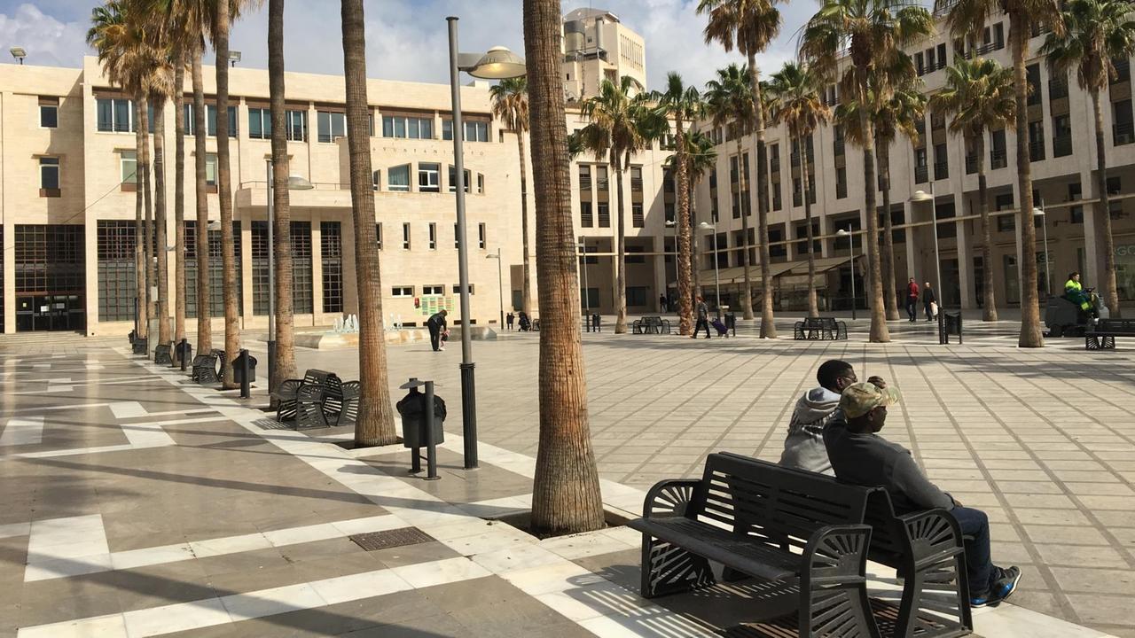 Der Rathausplatz von El Ejido, auf einer Bank sitzen zwei Menschen dunkler Hautfarbe.