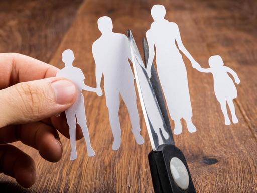 Ein Scherenschnitt von einem Elternpaar mit zwei Kindern wird von einer Schere in der Mitte durchgeschnitten
