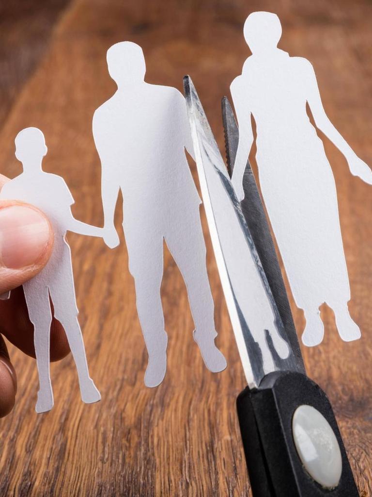 Ein Scherenschnitt von einem Elternpaar mit zwei Kindern wird von einer Schere in der Mitte durchgeschnitten