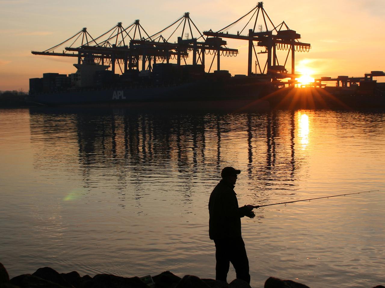 Ein Mann angelt am während des Sonnenuntergangs vor dem Container-Terminal Altenwerder (CTA) im Hamburger Hafen.