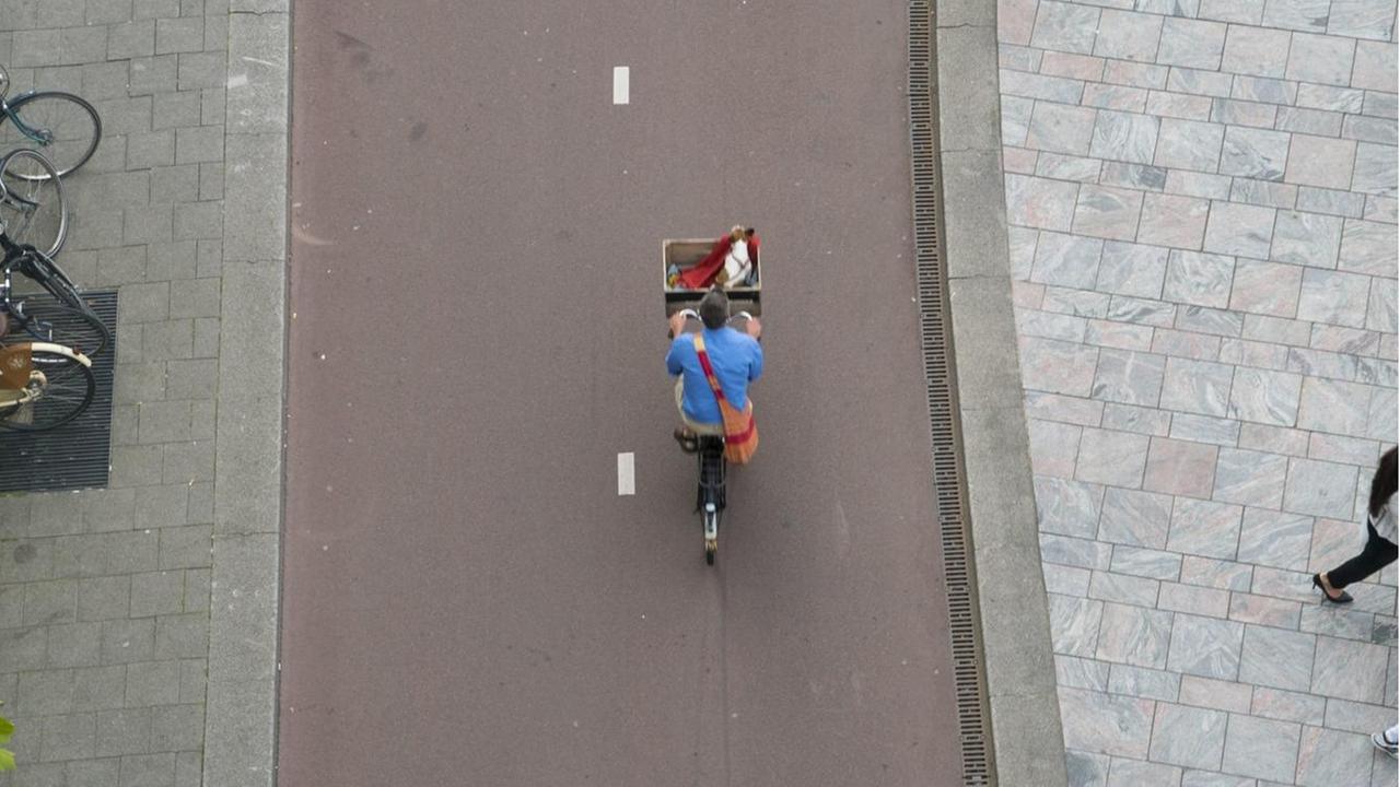 Ein Radfahrer wird aus der Vogelperspektive auf einem gut ausgebauten, rot geteerten Radweg gezeigt.