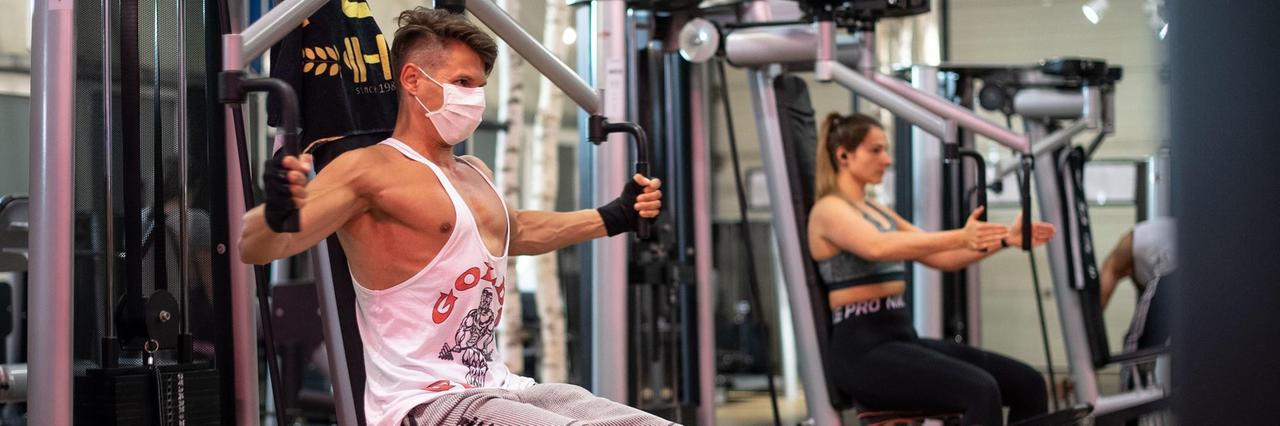 Ein Mann mit Mundschutz trainiert in einem Fitnessstudio an einer Brustpresse.