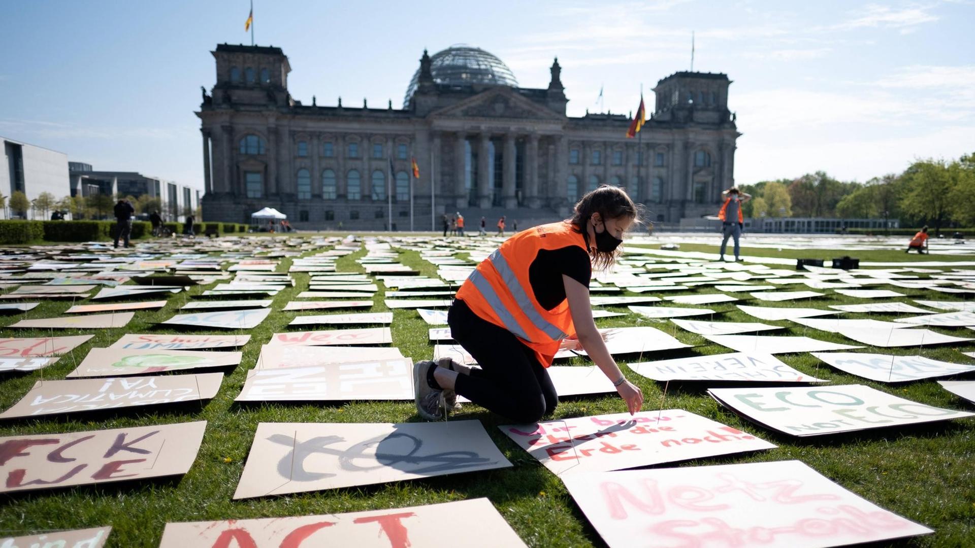 Im Vordergrund kniet eine Jugendliche auf der Wiese vor dem Reichstag. Sie legt ein Plakat aus. Um sie herum liegen tausende Plakate mit Aufschriften wie "Act now".