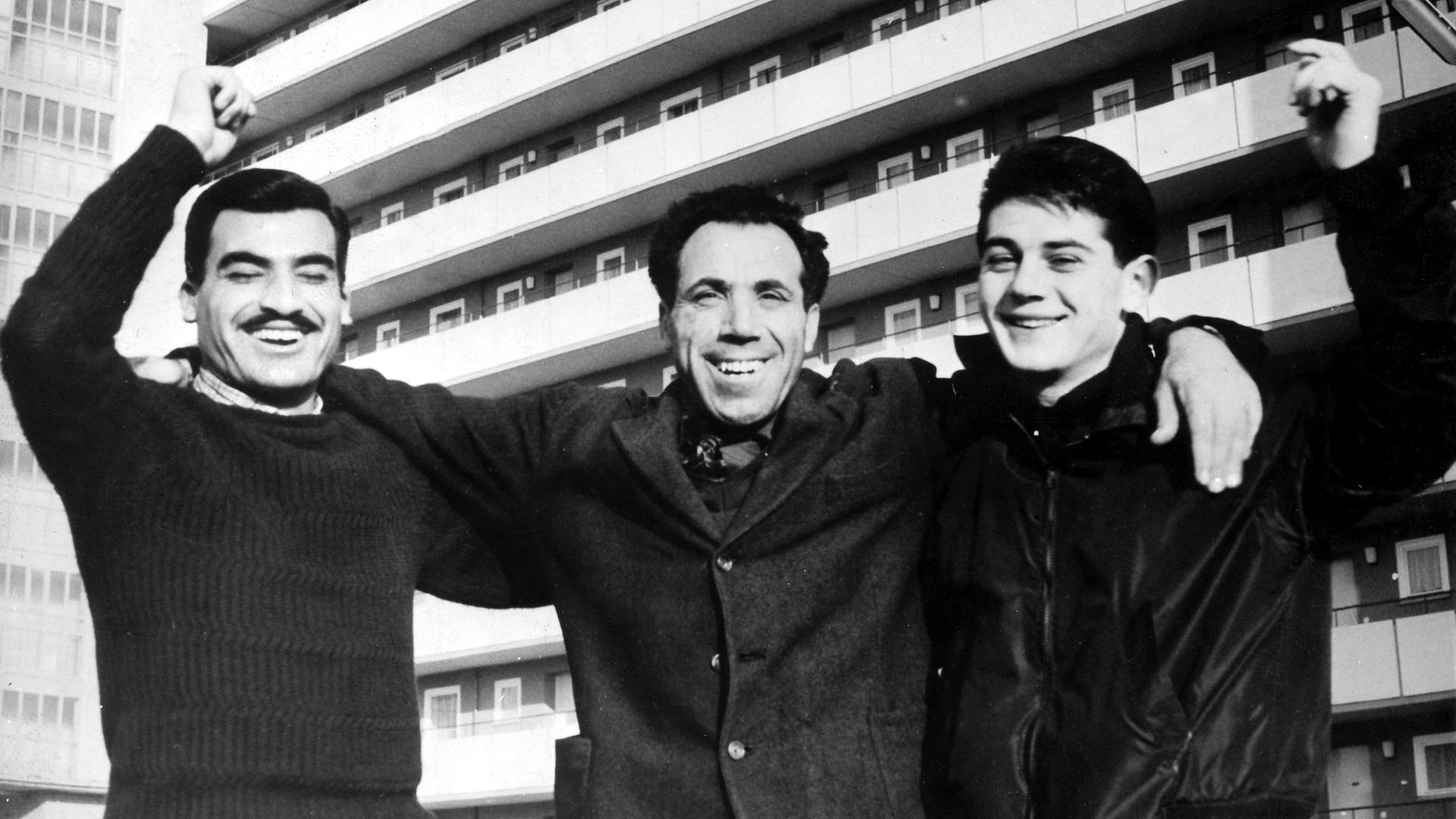 Lächelnd stehen drei italienische Gastarbeiter 1961 vor einem Junggesellenheim in Braunschweig