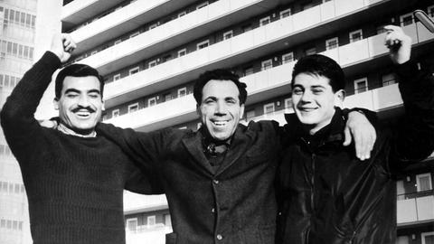 Lächelnd stehen drei italienische Gastarbeiter 1961 vor einem Hochhaus in Braunschweig. Schwarz-weiß-Aufnahme