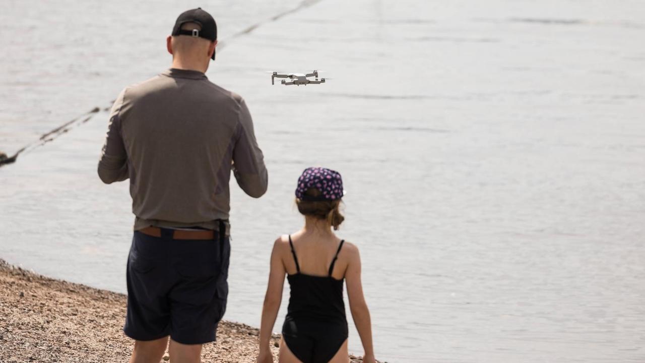Rückansicht von Vater und Tochter mit fliegender Drohne am Schluchsee