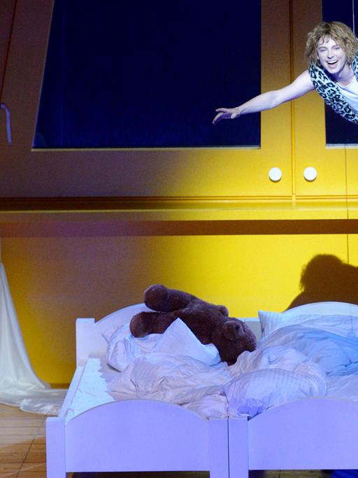 Zwei lila Betten stehen in einem gelben Zimmer. Links steht ein Mädchen und schaut auf zu einem, Jungen, der durch die Luft fliegt.
