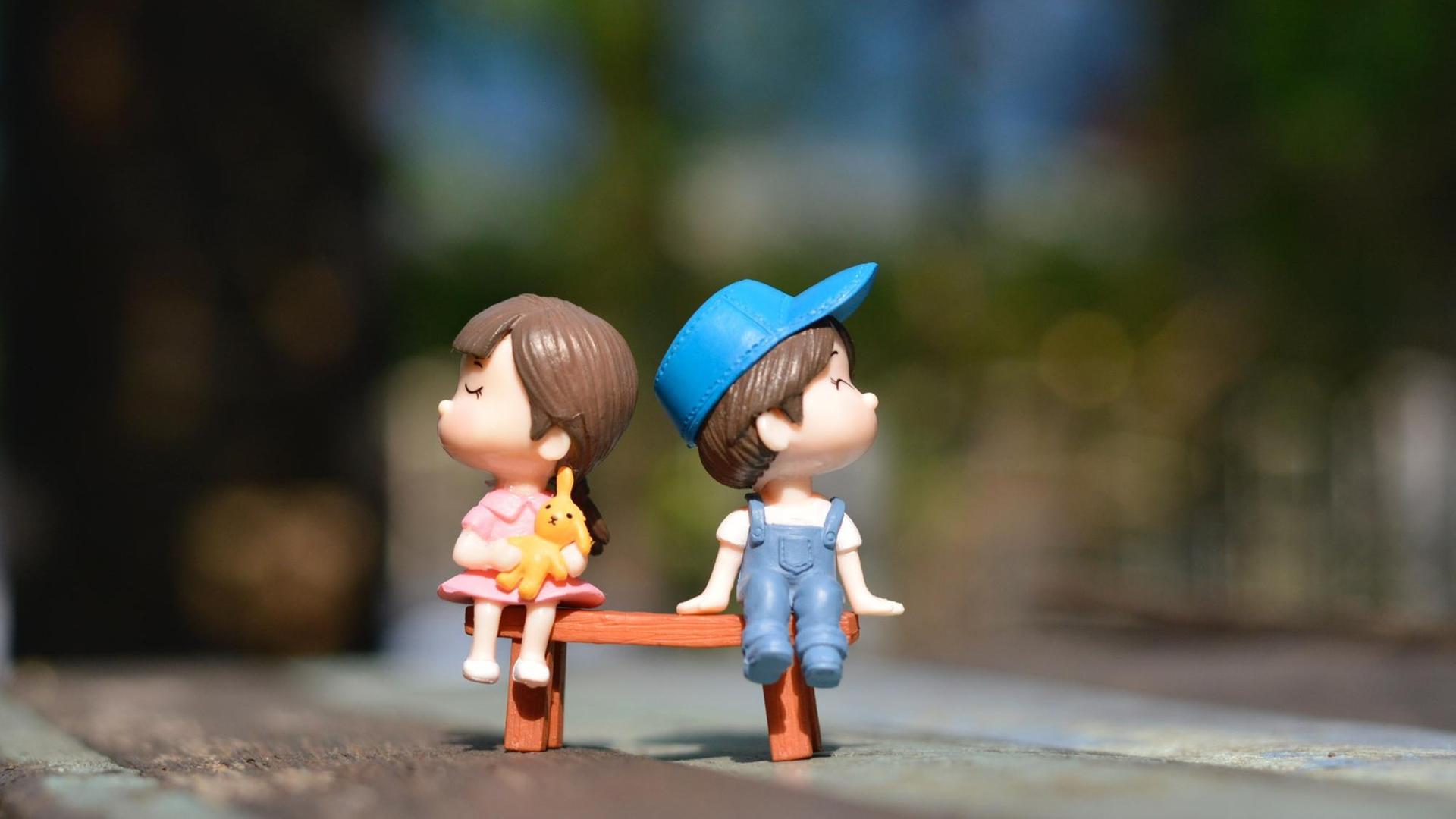 Zwei Kunststofffiguren, ein Junge und ein Mädchen, sitzen auf einer Bank.