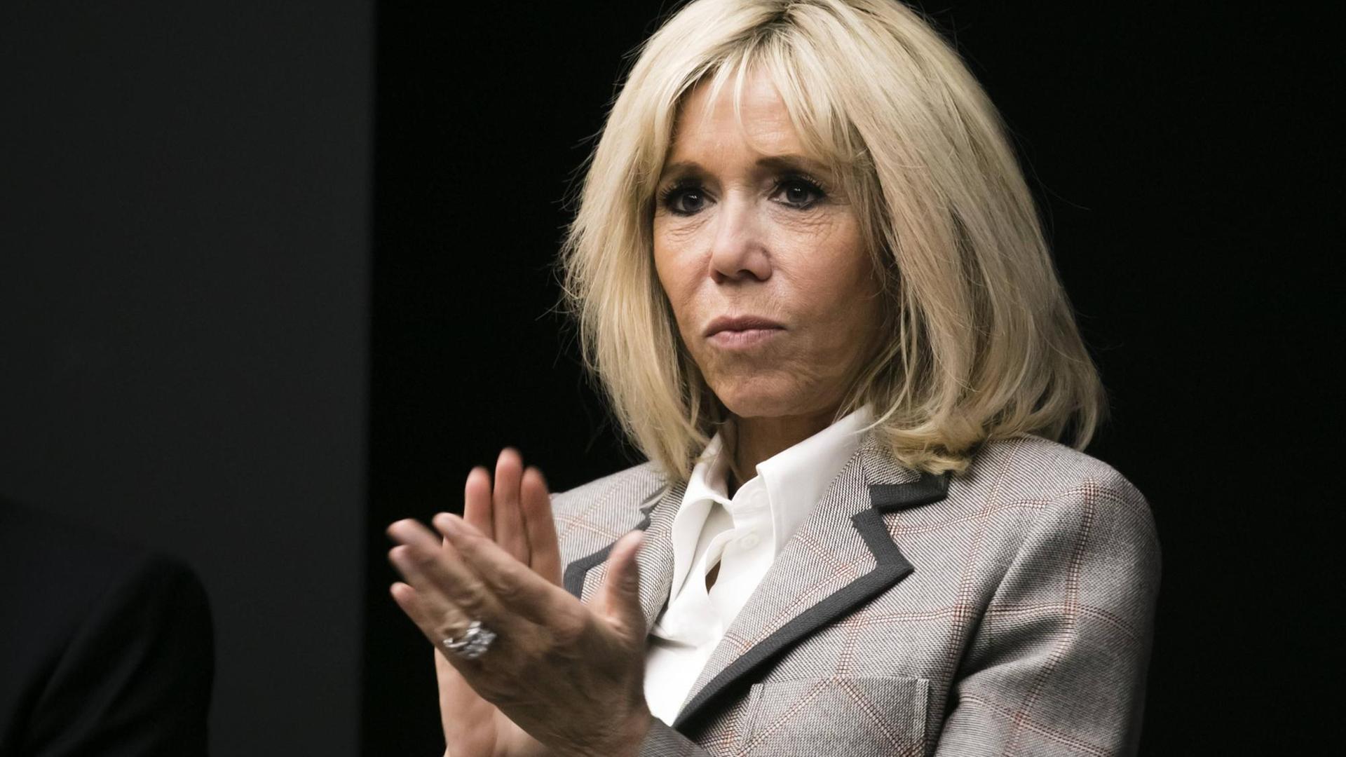 Macron im grauen Kostüm steht vor einem dunklen Hintergrund und klatscht in die Hände. Macron im grauen Kostüm steht vor einem dunklen Hintergrund und klatscht in die Hände.