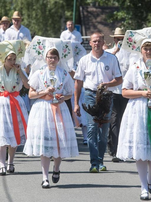 Junge Frauen und Männer in sorbischer Tracht nehmen im Spreewald am traditionellen Hahnrupfen teil.