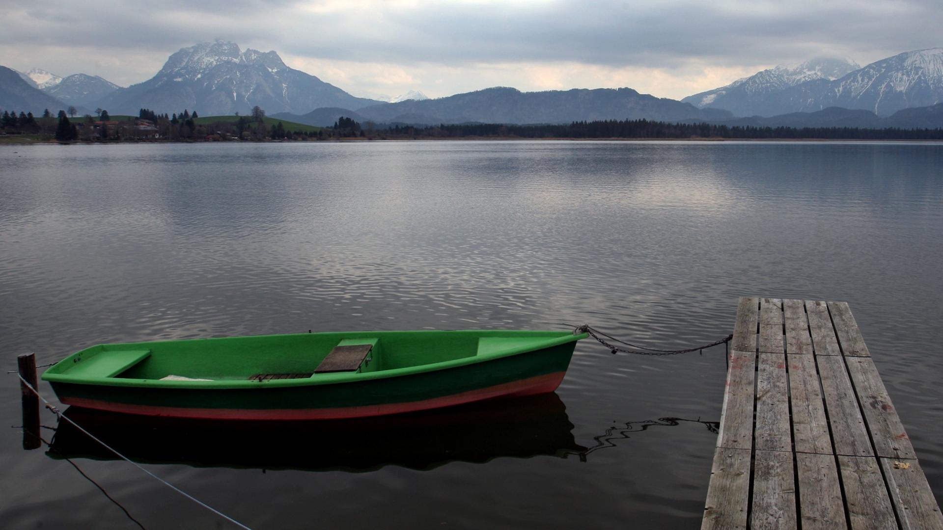 Wolkenverhangen ist es über einem See auf dem ein Holzboot an einem Steg liegt.