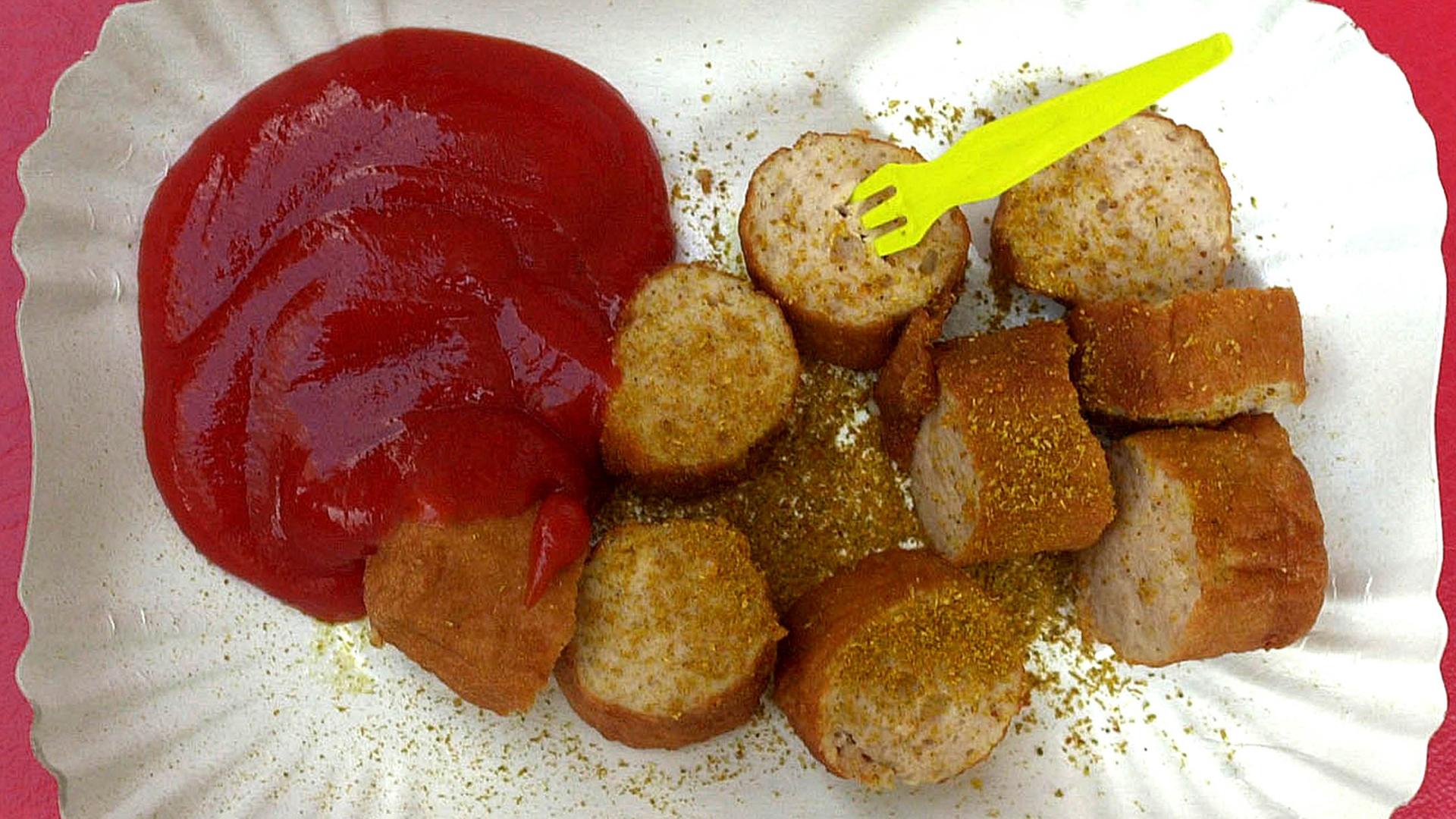 Ein Pappteller mit einer geschnittenen Currywurst, Curryketchup und einer Wurstgabel. Ein Pappteller mit einer geschnittenen Currywurst, Curryketchup und einer Wurstgabel.