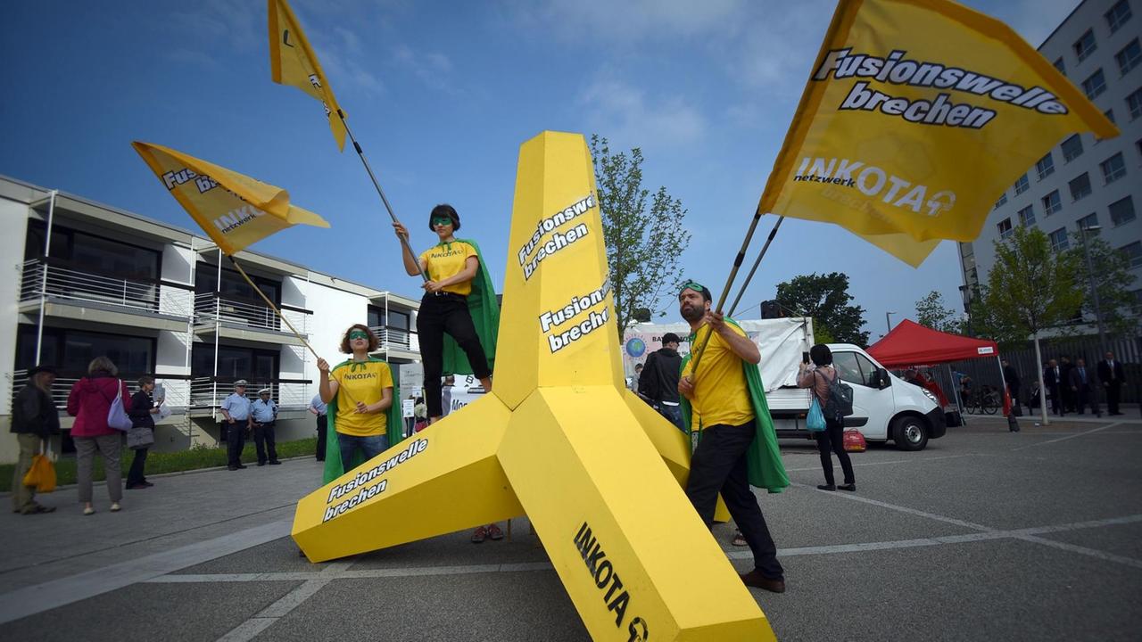 Demostranten mit gelben Fahnen stehen um und auf einem gelben Wellenbrecher