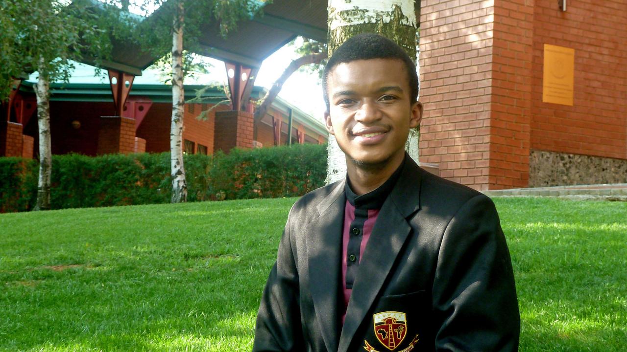 Ein junger Afrikaner steht in Schuluniform mit Jackett und Schulabzeichen auf dem Campusrasen.
