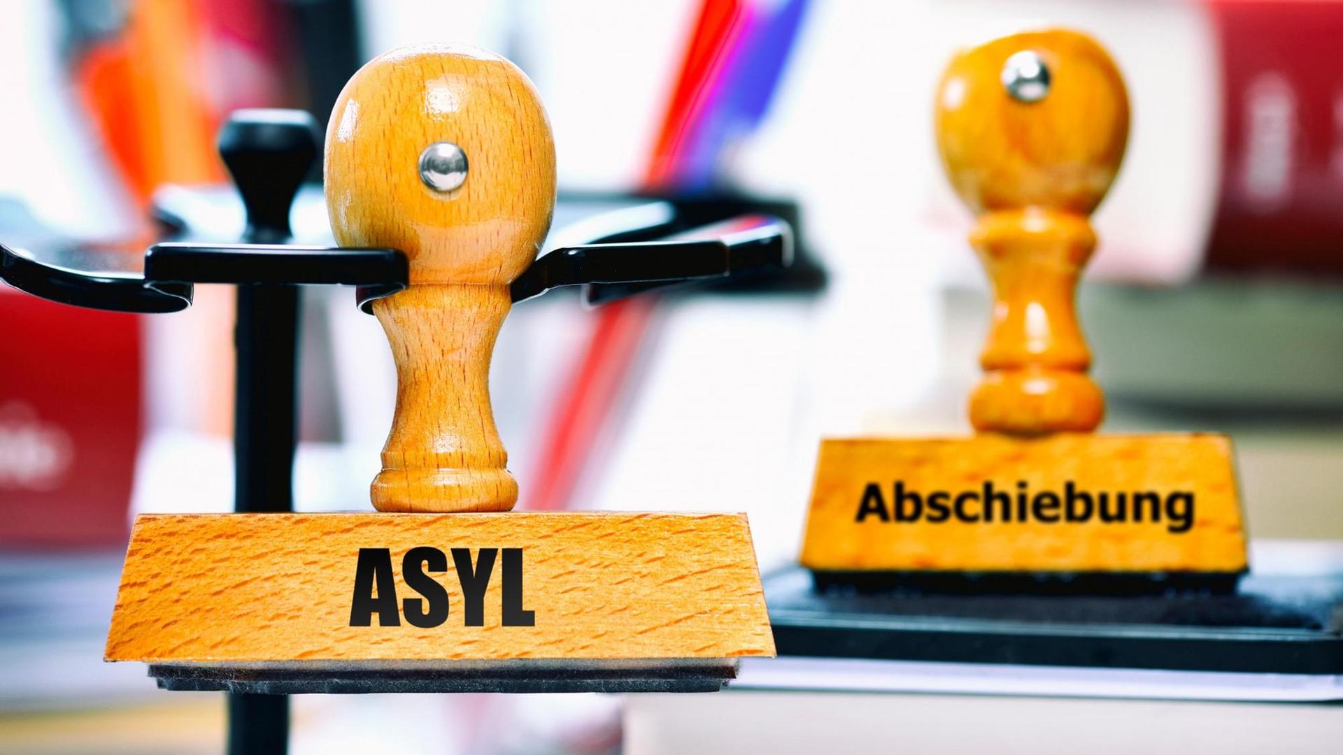 Auf einem Schreib-Tisch sind 2 Stempel mit den Worten "Asyl" und "Abschiebung".