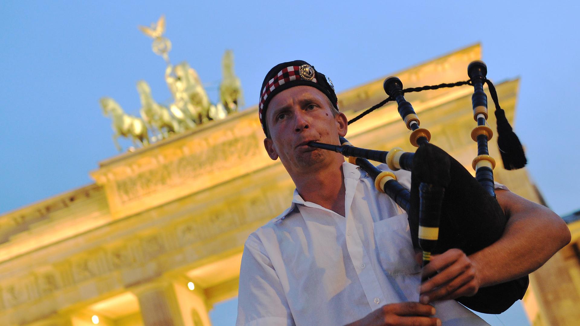 Ein Dudelsackspieler bläst vor dem erleuchteten Brandenburger Tor in sein Instrument.