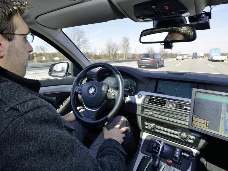 Ein Mann sitzt auf dem Fahrersitz eines Autos, das vom Bordcomputer gesteuert wird