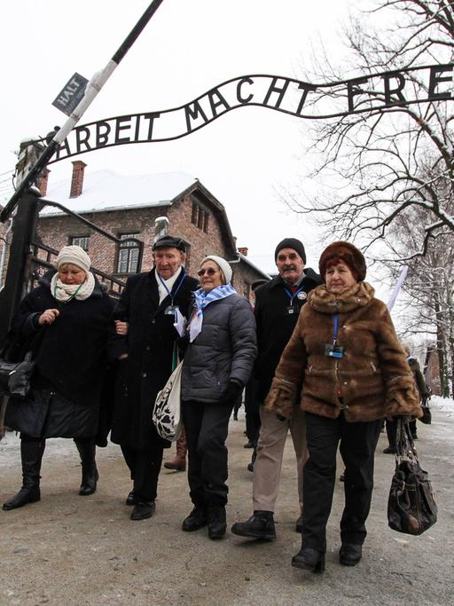 Überlebende des Konzentrationslagers Auschwitz vor dem Eingang mit dem Schriftzug "Arbeit macht frei".